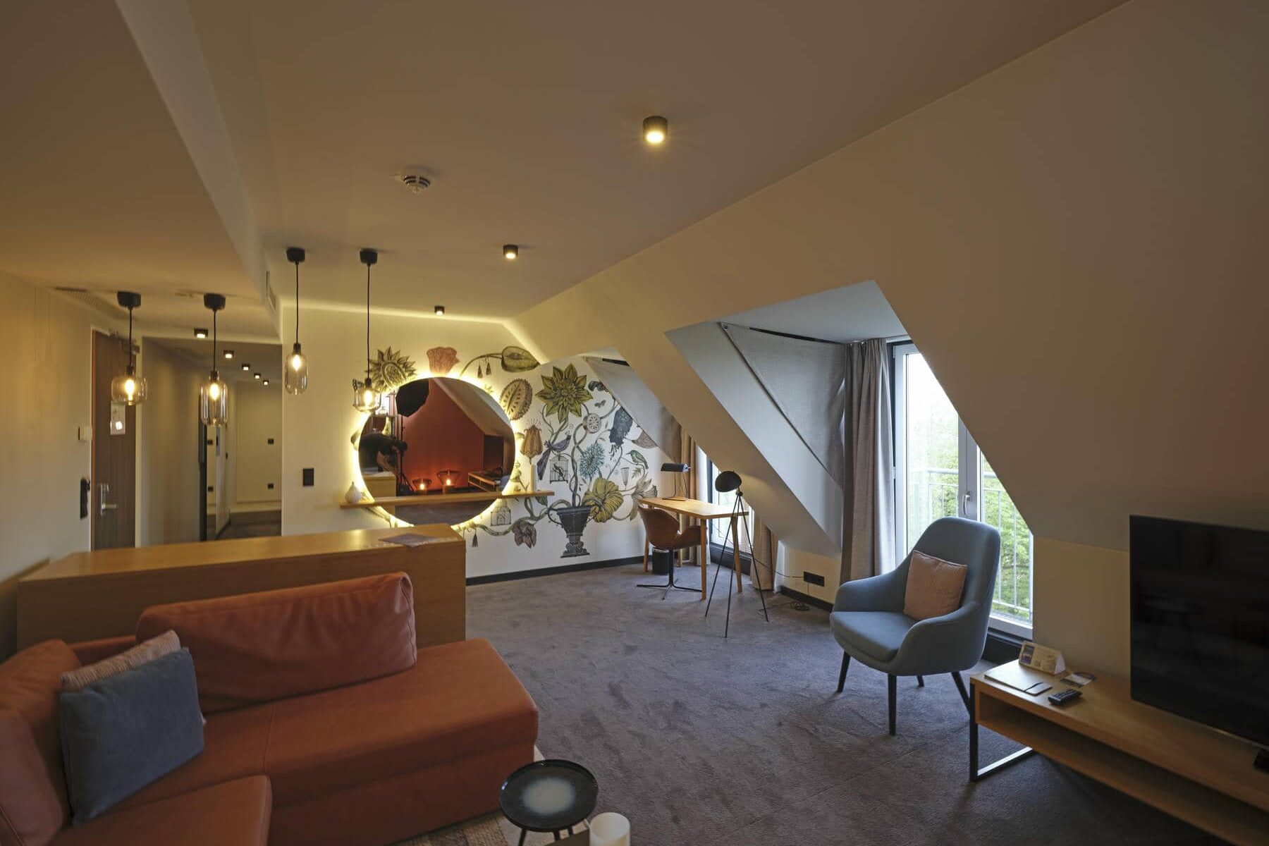 Wohnzimmer der Superior Suite mit großer Sofalandschaft, Bibliothek, Schreibtisch, gemütlichen Dachschrägen und modernem Lichtkonzept
